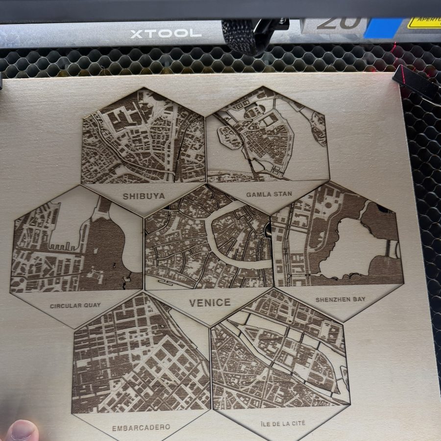 Seven hex tiles freshly engraved on a sheet of plywood inside an xTool laser.