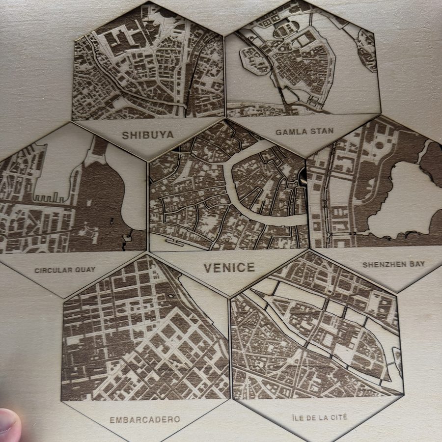 Seven laser-engraved hexagon map tiles fitted together: Shibuya, Gamla Stan, Circular Quay, Venice, Shenzhen Bay, Embarcadero and Île de la Cité.